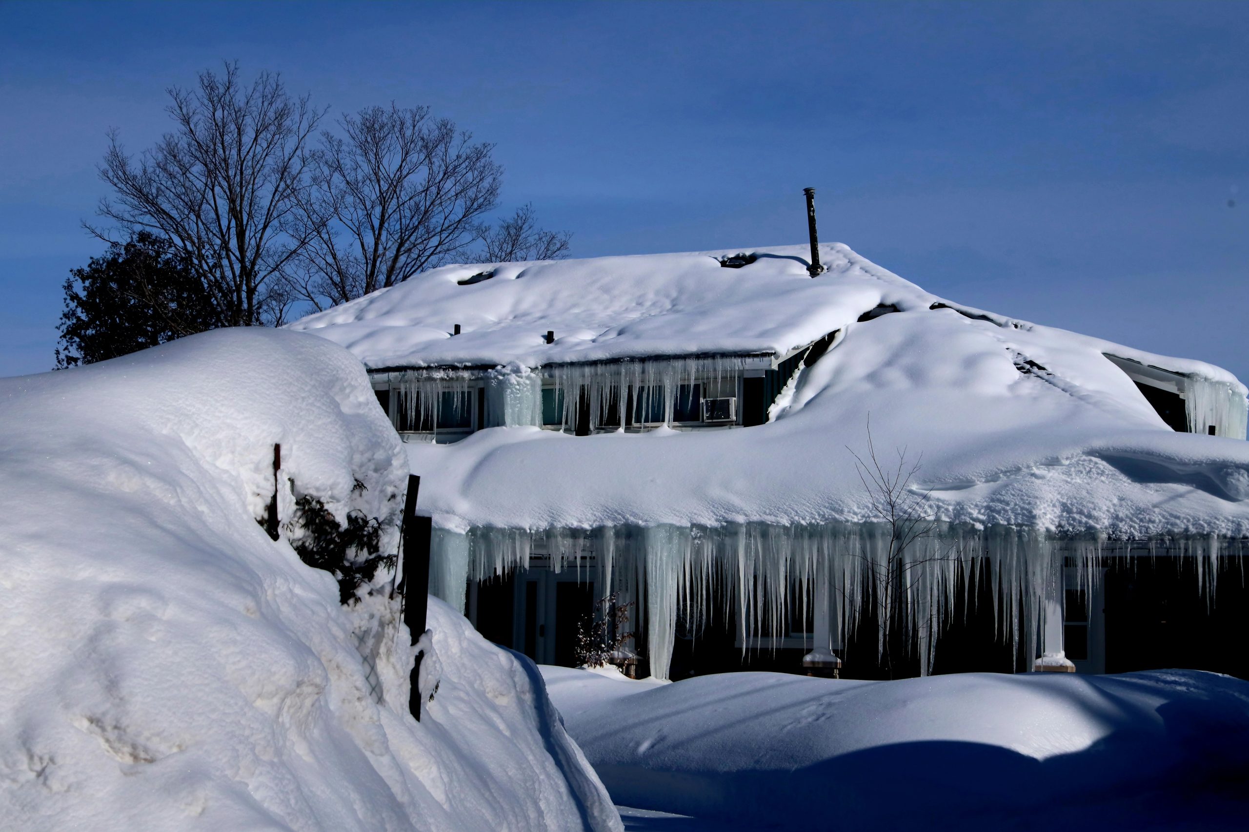 A rural property buried in snow with icicles hanging from the roofline, the kind of winter weather that can bring on a power outage